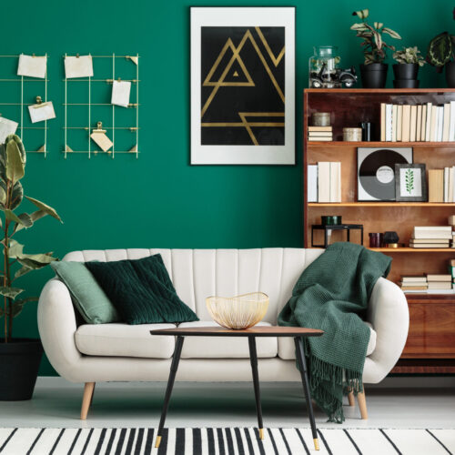 Cozy, designer living room interior with a home library, antique wooden bookcase, beige sofa and modern, abstract art on a teal green wall